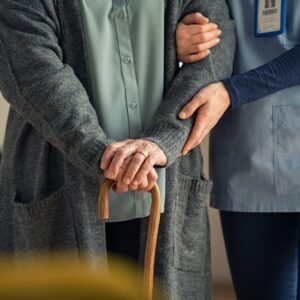 nurse helps support a woman holding cane 