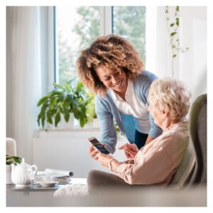 nurse holds phone to older woman sitting in chair
