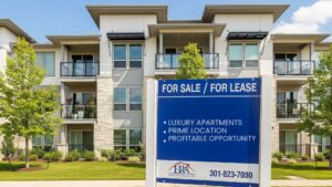 A large, modern multifamily apartment building with a commercial for-sale sign placed in the front.