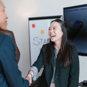 Two businesswomen smiling and shaking hands in an office setting.