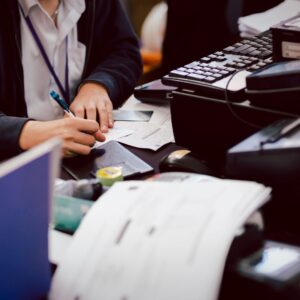 Close-up of hands writing on paper next to a keyboard and various office documents.