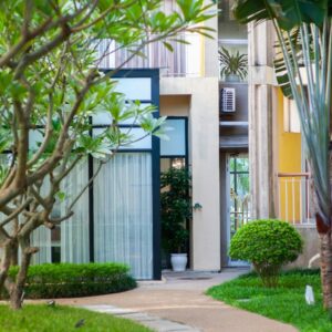 A winding garden path leading towards a modern building entrance, surrounded by lush greenery and trees.