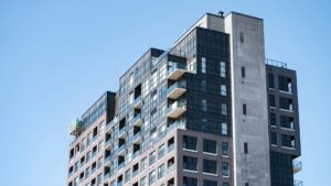 A modern, multi-story apartment building with balconies and large windows against a clear blue sky.