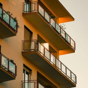 A low-angle architectural shot of several sleek, modern apartment balconies with glass railings, emphasizing the scale and repetitive structure of a large multifamily complex.