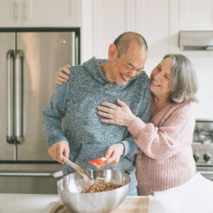 A happy senior couple laughing together in a modern kitchen while preparing food, illustrating the vitality and joy of active aging.